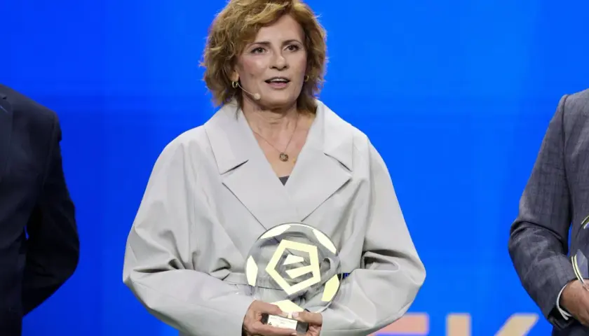 Kobieta w jasnym płaszczu trzyma szklaną statuetkę w kształcie piłki nożnej.