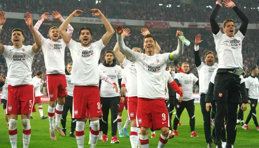 Piłkarze reprezentacji Polski w białych koszulkach i czerwonych spodenkach świętują na boisku.